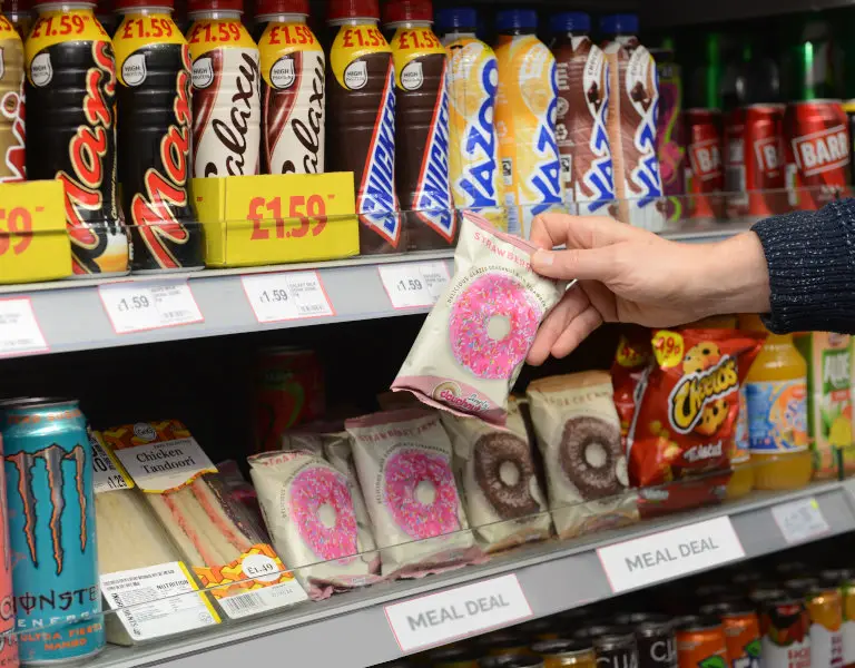 A shopper picking up a Simply Doughnuts pack from a meal deal shelf