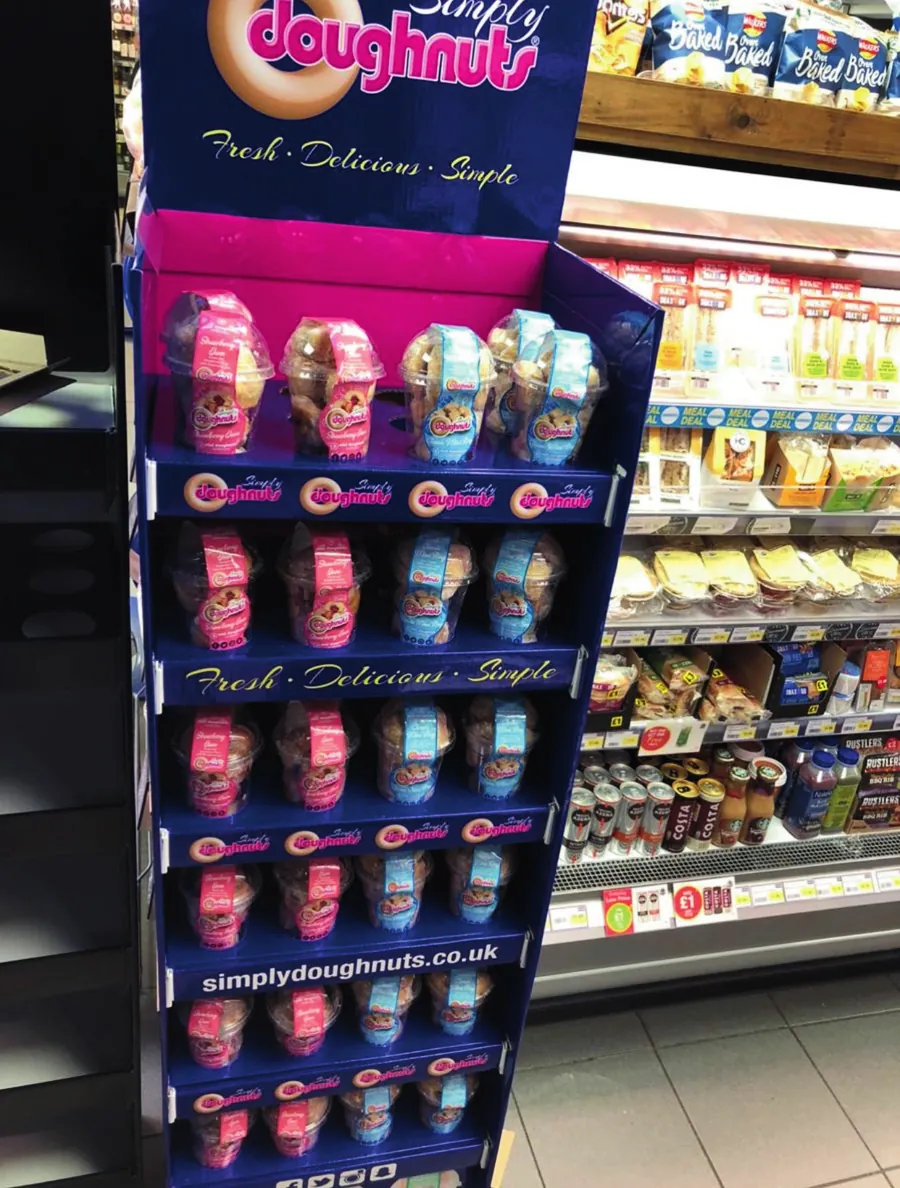 A branded Simply Doughnuts floor display unit filled with packs in a convenience store